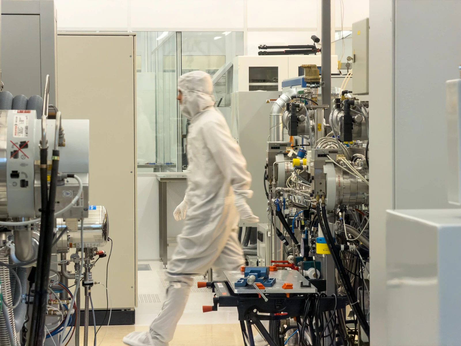 A person in cleanroom clothing walking between nanofabrication equipment at Chalmers.